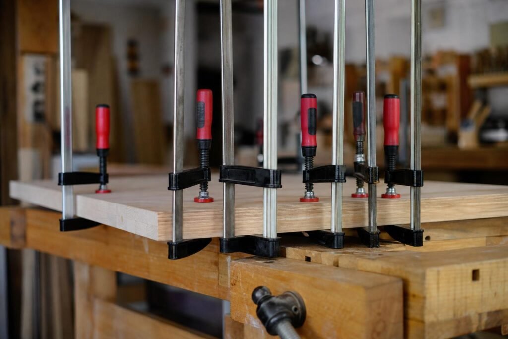 Plusieurs serre-joints de menuisier serrant un panneau de bois collé sur un établi